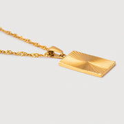 Gold necklace with a rectangular pendant worn by a person in a yellow top.