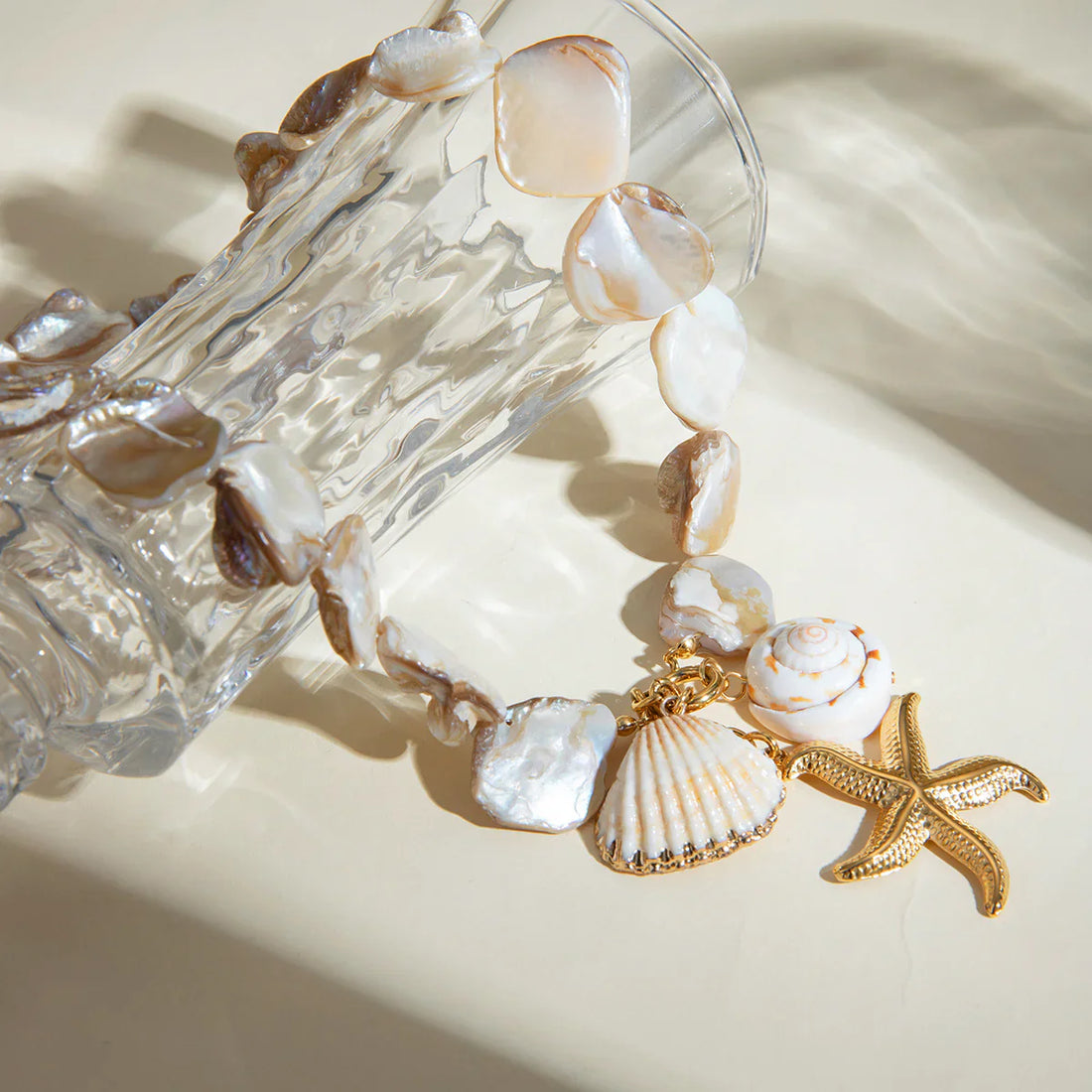 Bracelet with shell and starfish charms on a glass container with shells.