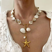 Necklace with shell and starfish charms worn by a person in a white lace top.