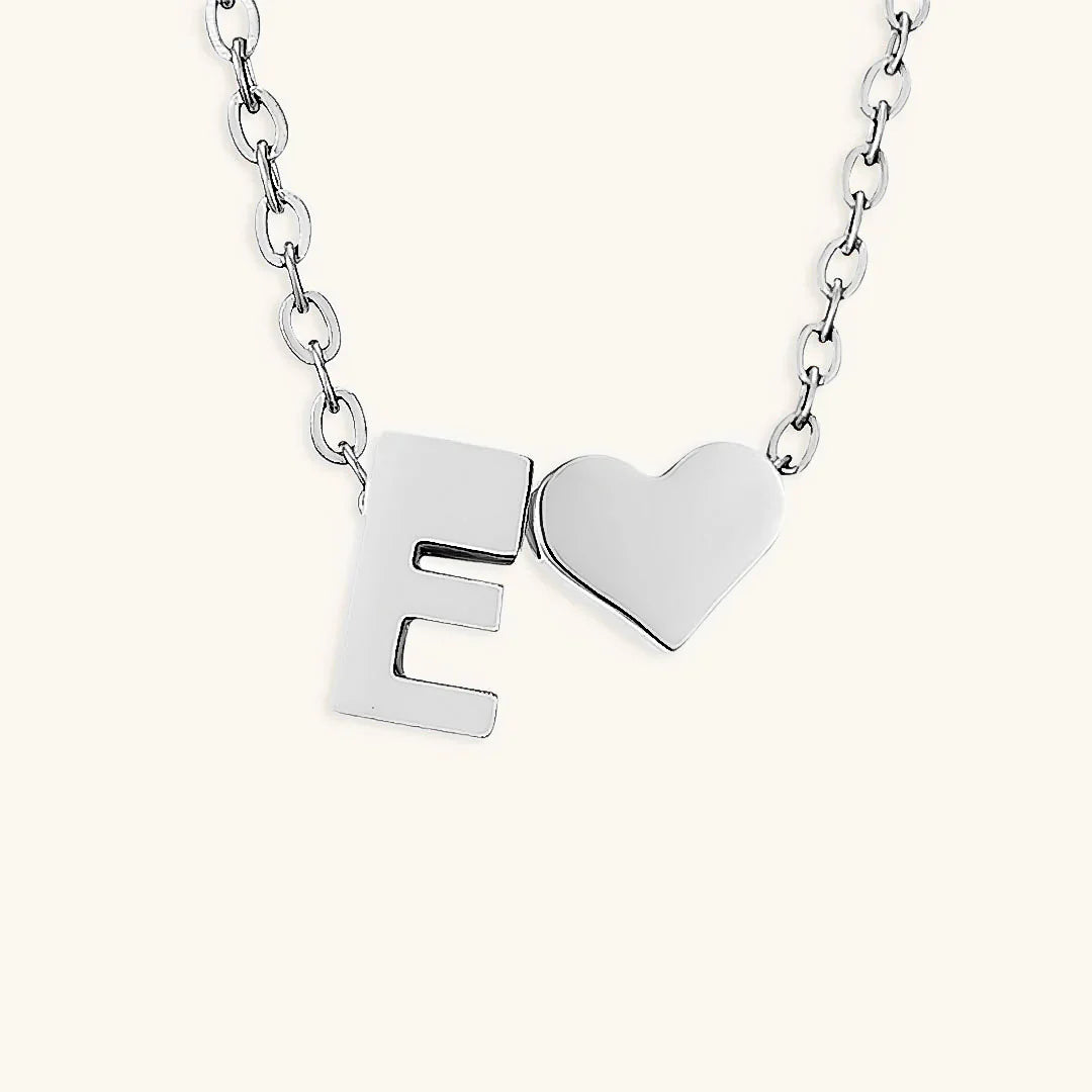 Silver necklace with letter 'E' and heart pendant on a white background