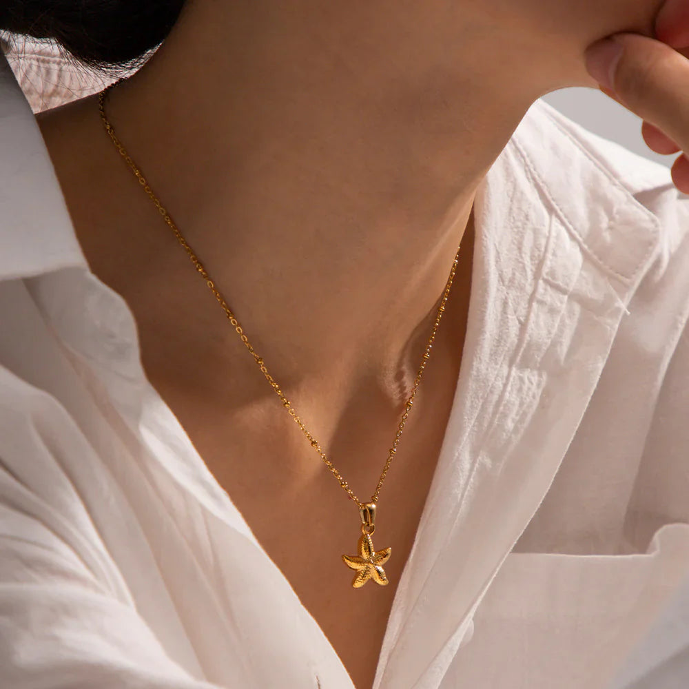 Gold necklace with a starfish pendant worn by a person in a white shirt.