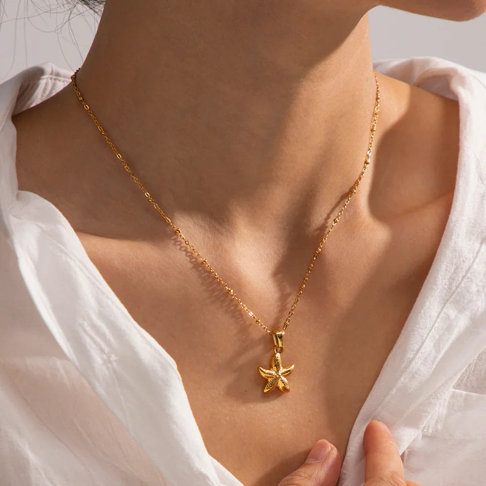 Gold necklace with a starfish pendant worn by a person in a white shirt.