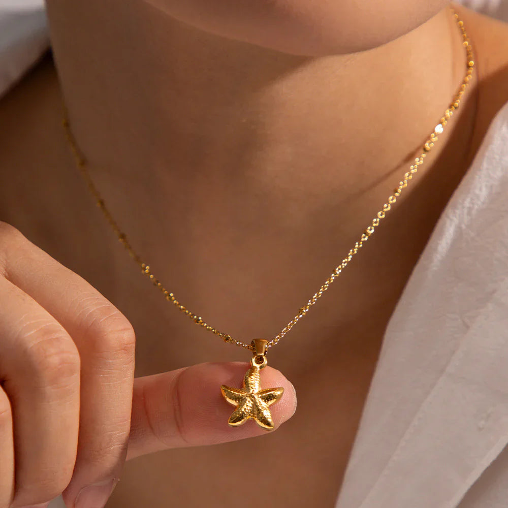 Gold necklace with a starfish pendant held by a hand